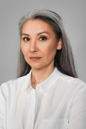 portrait of middle aged woman with gray hair looking at camera isolated on gray