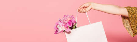 cropped view of woman holding white shopping bag with peonies isolated on pink, bannerの写真素材