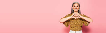 smiling woman showing heart sign with hands on pink background, banner