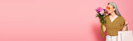 middle aged woman with shopping bag smelling fresh peonies on pink background, bannerの写真素材