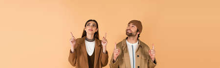 stylish couple in autumn outfit pointing up with fingers isolated on beige, bannerの写真素材