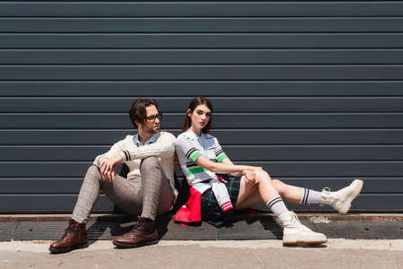 young fashionable couple sitting on border near gray wall outdoorsの写真素材