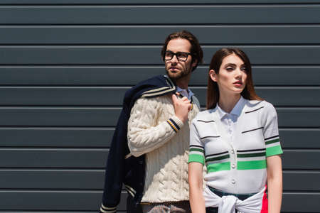 trendy couple in stylish clothes standing near gray wall outdoors