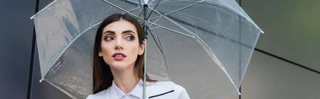 pretty brunette woman looking away under transparent umbrella, bannerの写真素材
