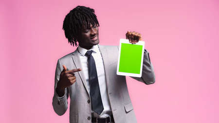 happy african american businessman pointing at digital tablet isolated on pinkの写真素材