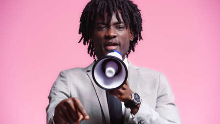 african american businessman speaking into loudspeaker isolated on pink
