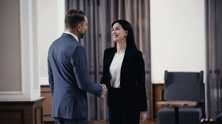 cheerful businesswoman shaking hands with businessman in lobby of restaurant