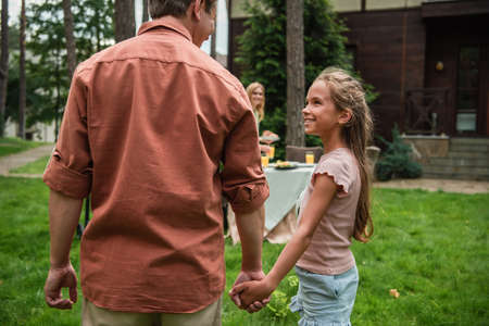 Smiling kid with football ball holding hand of father outdoors