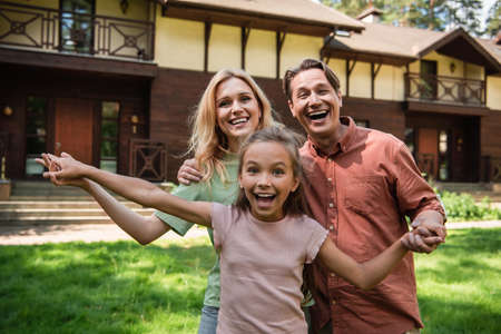 Cheerful kid looking at camera near parents and vacation houseの写真素材