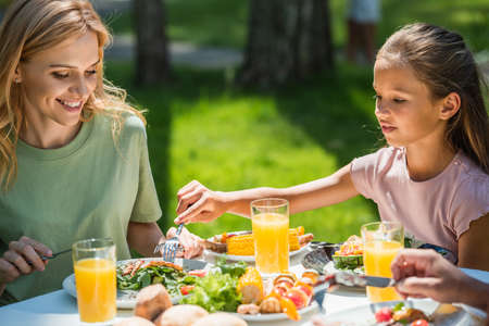 Smiling woman sitting near kid with fork and food during picnic outdoorsの写真素材