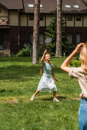 Smiling kid playing badminton near mother on lawnの写真素材