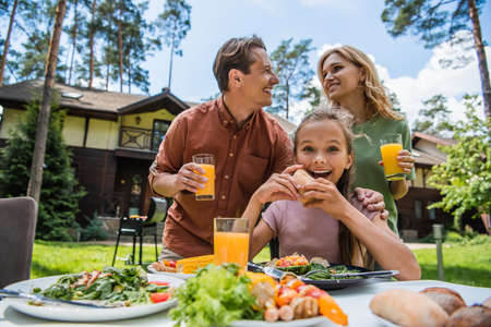 Positive kid looking at camera near food and parents outdoorsの写真素材