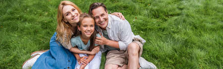 High angle view of parents hugging smiling kid on grass, banner