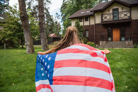 Back view of girl holding american flag while running on lawnの写真素材