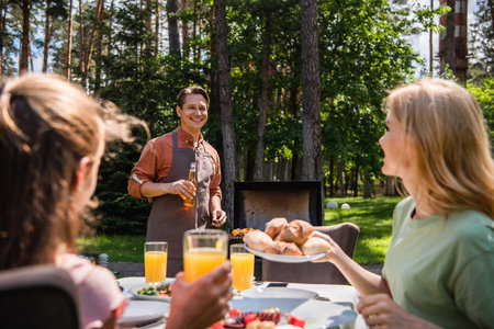 Smiling man with beer standing near blurred wife with buns and child with orange juice outdoorsの写真素材
