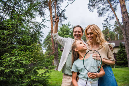 Positive family with badminton rackets hugging outdoors