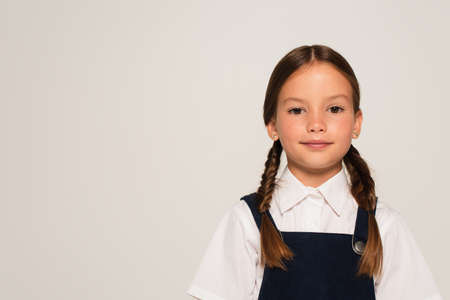 positive girl in school uniform looking at camera isolated on gray