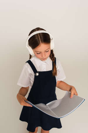 girl in headphones and school uniform reading copy book isolated on gray