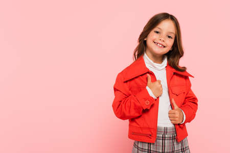 cheerful girl in orange jacket smiling at camera isolated on pinkの写真素材
