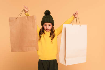 fashionable girl in yellow turtleneck standing with shopping bags in raised hands isolated on beigeの写真素材