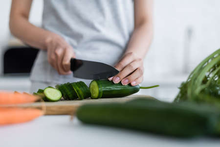 partial view of woman cutting fresh cucumber on blurred foregroundの写真素材