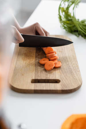 cropped view of woman cutting fresh carrot on chopping board, blurred foreground