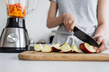 cropped view of blurred woman cutting apple on chopping board near electric shakerの写真素材