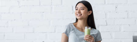 young asian woman with glass of fresh smoothie smiling while looking away, bannerの写真素材