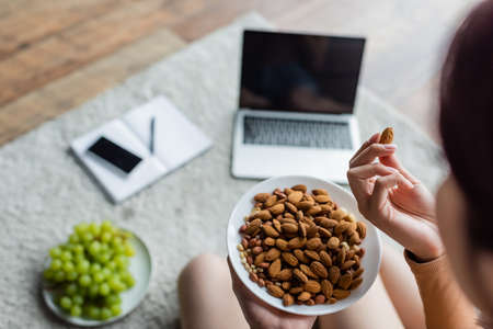 cropped view of woman eating almonds near blurred gadgets and fresh grape on floorの写真素材