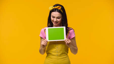 Happy woman looking at digital tablet with green screen isolated on yellowの写真素材