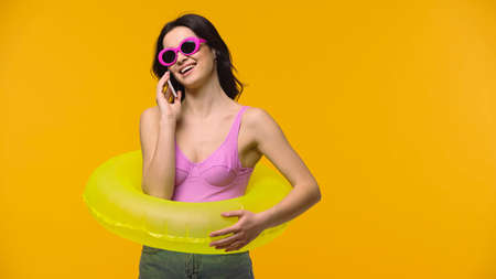 Woman in swimsuit and sunglasses talking on smartphone isolated on yellowの写真素材