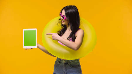 Side view of smiling woman in swim ring pointing at digital tablet with chroma key isolated on...