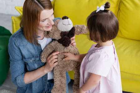 happy kindergarten teacher holding teddy bear near kid with down syndromeの写真素材