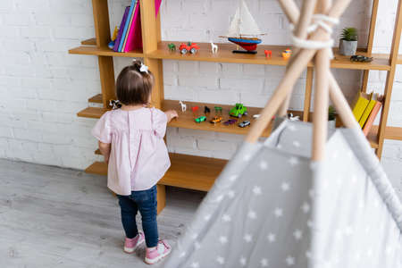 back view of toddler girl with down syndrome reaching toys on wooden shelfの写真素材