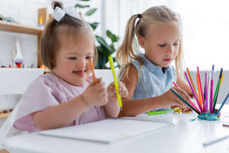 girl taking pink pencil near blurred disabled kid with down syndromeの写真素材