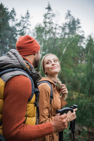 happy young couple with backpacks trekking together with hiking sticks and looking at each otherの写真素材