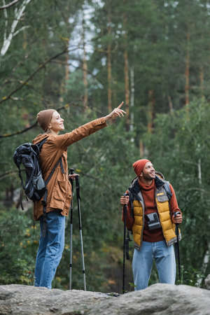 happy woman pointing with finger near boyfriend trekking in forestの写真素材