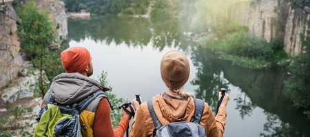 back view of couple with backpacks near lake in forest, bannerの写真素材