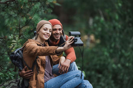 cheerful couple taking selfie on vintage camera in forestの写真素材