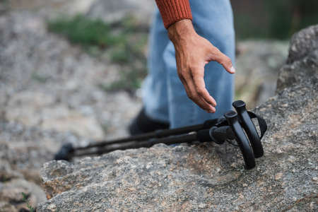 cropped view of man reaching hiking sticks on rockの写真素材