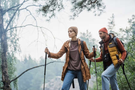 couple in hats holding hiking sticks while trekking in forestの写真素材