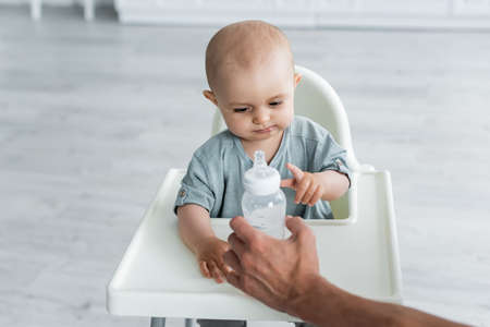 Father holding bottle with water near baby on high chairの写真素材