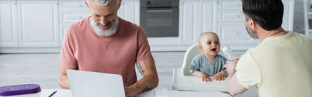 Homosexual freelancer using laptop near partner and daughter, banner