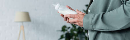 Cropped view of man holding baby bottle with milk, bannerの写真素材