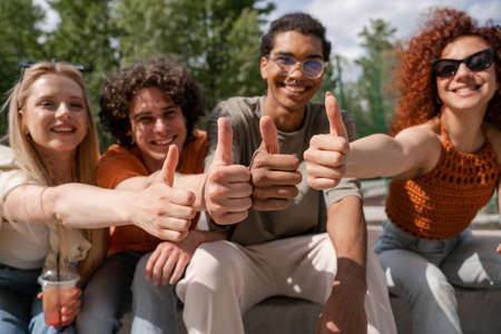 blurred multiethnic friends smiling and showing thumbs up in city parkの写真素材