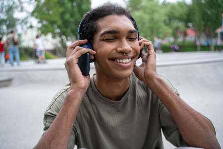 pleased african american man listening music in wireless headphones in city parkの写真素材