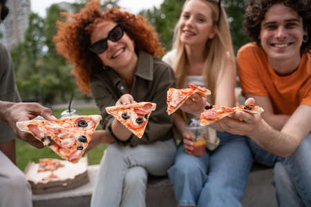blurred multicultural friends smiling while showing pieces of tasty pizzaの写真素材