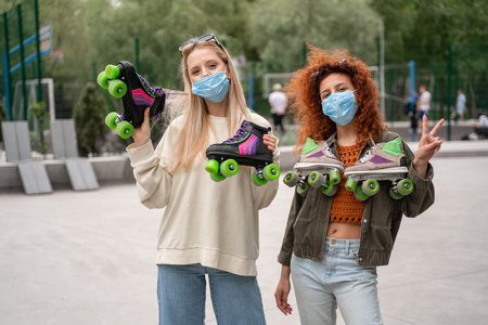 young roller skaters in medical masks looking at camera outdoors
