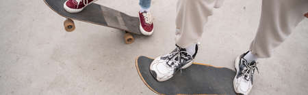 partial view of men in sneakers riding skateboards outdoors, banner