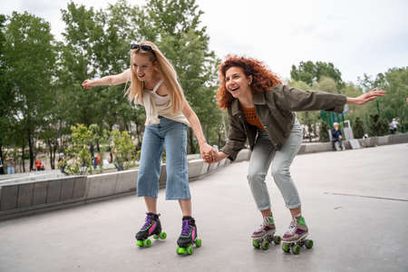 excited women holding hands while rollerblading in parkの写真素材
